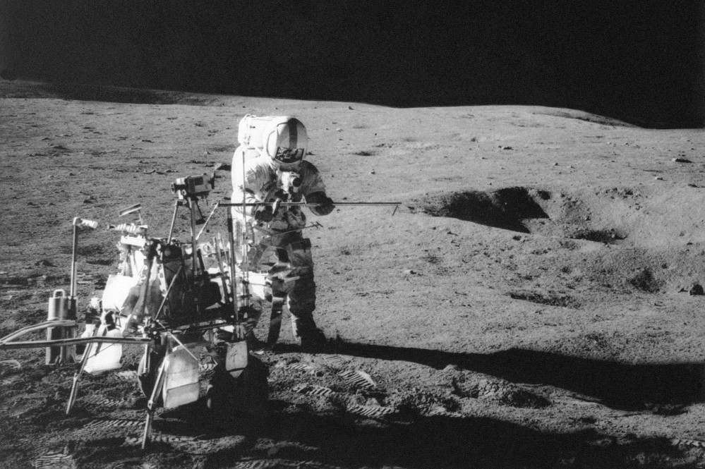 Apollo 14 astronaut Alan B. Shepard Jr. conducts an experiment near a lunar crater, using an instrument from a two-wheeled cart carrying various tools. Analysis of material collected on that trip has led a research team to conclude that the moon formed within 60 million years of the birth of the solar system.