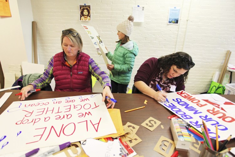 Kristen Farnham, left, and her daughter Audrey, 9, work alongside Beth Penrose as people prepare signs to carry at a protest of the inauguration of President-elect Donald Trump. 