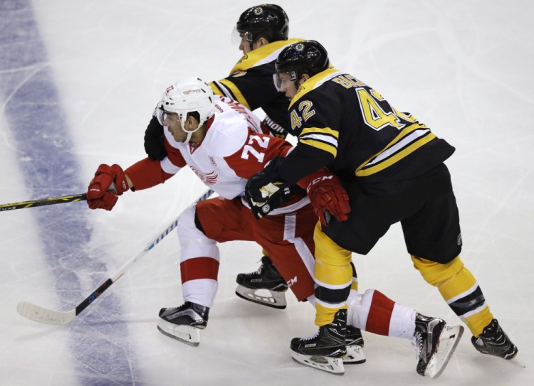 Red Wings center Andreas Athanasiou is held back by Boston’s David Backes, right, and Frank Vatrano in the first period Tuesday night in Boston.
