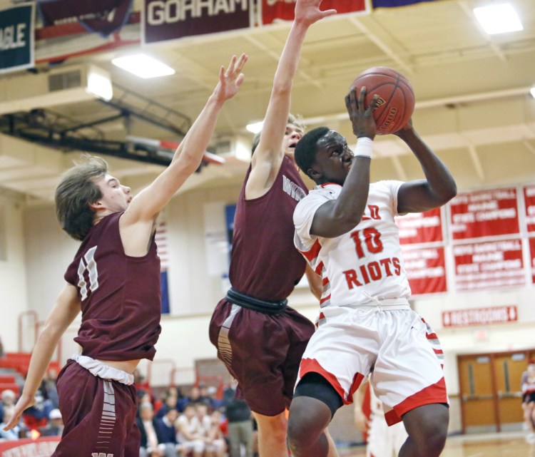 Moses Oreste of South Portland drives to the basket past Windham's Hunter Coffin, left, and Nicholas Curtis during the Red Riots' 62-53 win Tuesday in South Portland.