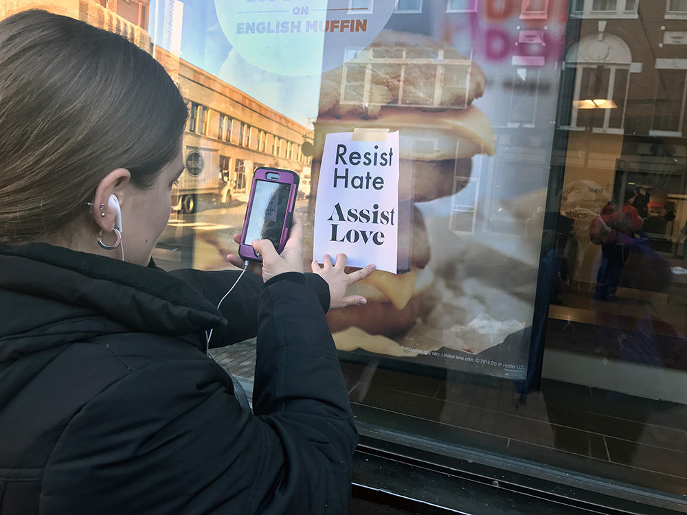 Sarah Muehle of Portland takes a photo of one of the signs that appeared in storefronts along Congress Street Friday morning.