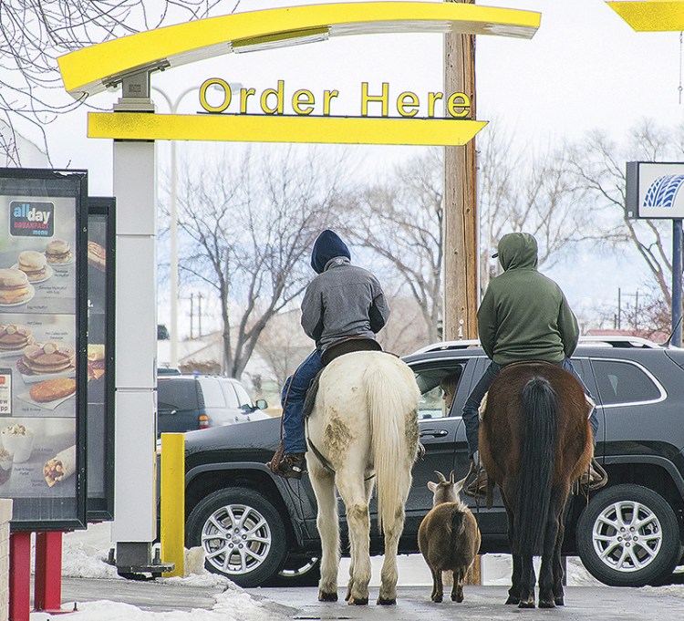 Trajen Collins, left, is joined by Joel Perez as they ride their horses through the McDonald's drive-thru with a pet goat in tow in Powell, Wyo. 