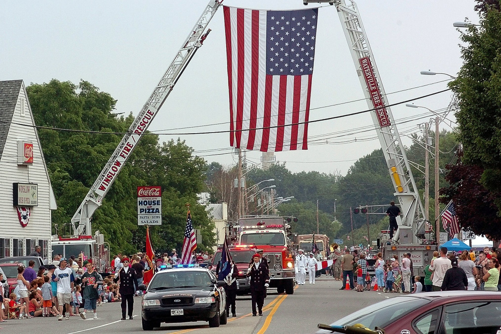 Participants in a previous Winslow Fourth of July parade pass under a huge American flag on Bay Street suspended by ladder trucks from the Winslow and Waterville fire departments. Event organizers aren't sure where the celebration will be held this year, if at all.