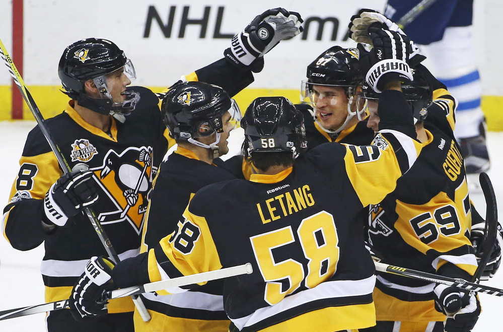 Sidney Crosby, rear, is surrounded by Penguins teammates after he earned his 1,000 career point by assisting on a goal by Chris Kunitz in the first period Thursday night. Crosby added another assist, and then scored in overtime to deliver Pittsburgh a 4-3 win at home against the Winnipeg Jets.