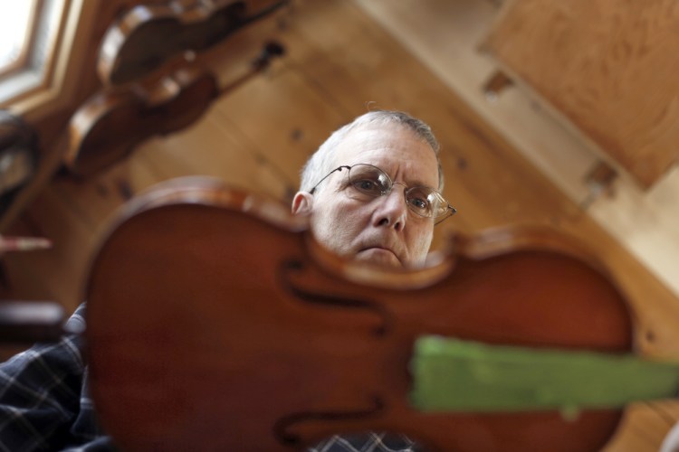 Don Roy checks his work after varnishing a work-in-progress fiddle in his Gorham shop.