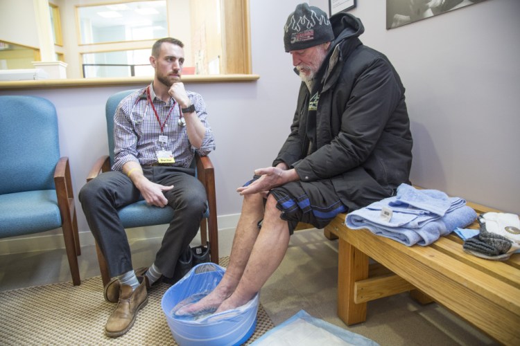 Dr. Adam Normandin listens to Brian French at the 20 Portland St. clinic as the homeless man bathes his feet in warm water and Epsom salt to treat symptoms of frostbite.