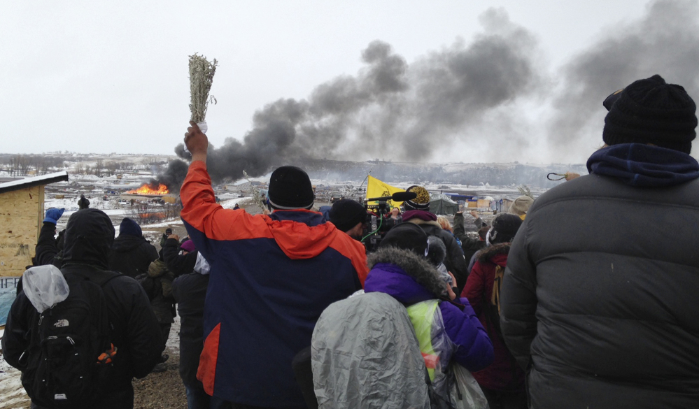 A fire burns in the background as opponents of the Dakota Access pipeline leave their protest camp near Cannon Ball, N.D. on Wednesday. Authorities were preparing to shut down the camp before spring flooding season.