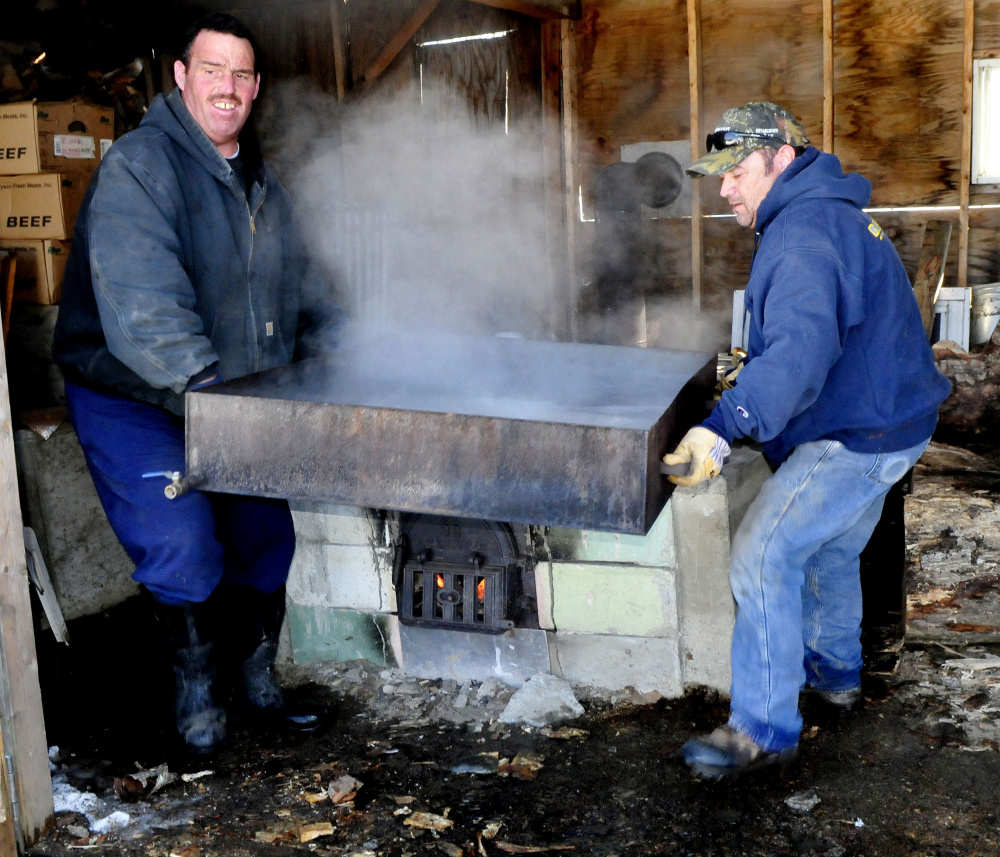 Paul Elkins, left, and Kurt Parker lift a tray of boiling maple syrup off the fire pit at their sap house in Thorndike on Thursday. Maine syrup makers are getting an early start on the season as warm temperatures have caused sap to start running. At a recent Maple Producers Association meeting, about half the members said they'd already started tapping and making syrup, while the other half is gearing up to start soon. Last year, producers in southern Maine were tapping in January, the earliest many could remember doing so.  