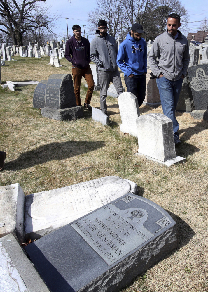 Volunteers from the Ahmadiyya Muslim Community survey damaged headstones at Mount Carmel Cemetery in Philadelphia on Monday. More than 100 headstones have been vandalized at the Jewish cemetery.