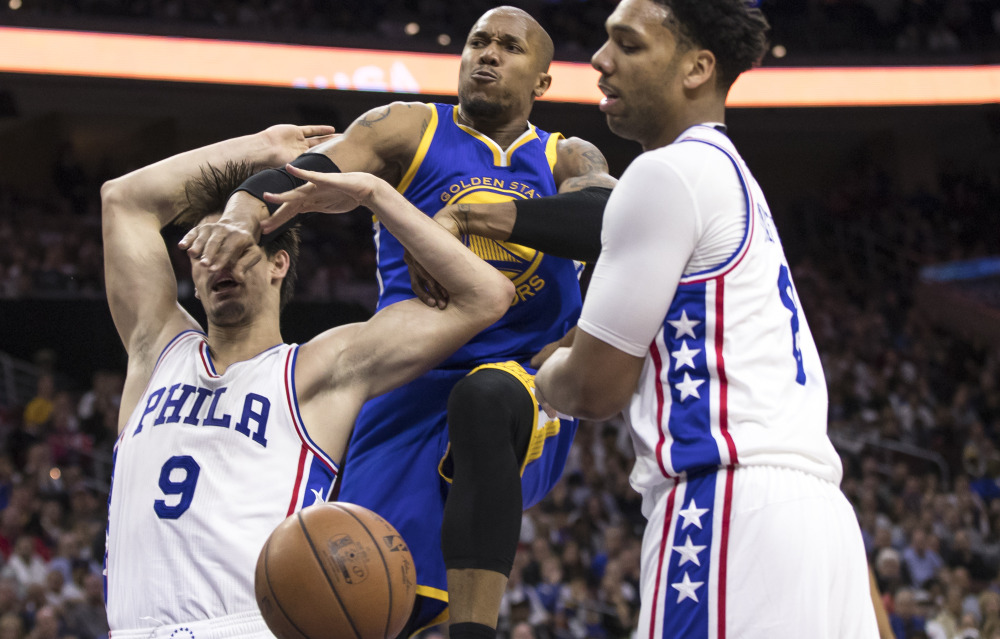 Golden State's David West, center, hits Philadelphia's Dario Saric, left, from behind while Jahlil Okafor reaches in Monday in Philadelphia. West was called for a flagrant foul on the play, but the Warriors won 119-108.
