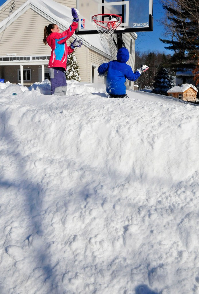 Standing on a 6-foot-tall snowbank, Avery Willett, left, and her brother, Hunter, slam dunk snowballs in a basketball hoop at their home in Waterville on Tuesday. The kids had the day off from school because of the latest winter storm.