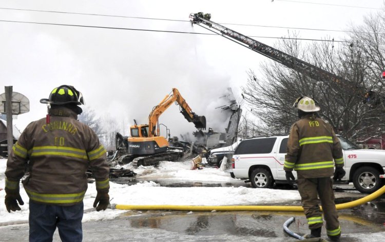 Firefighters from the Skowhegan Fire Department spray water from a ladder truck as an excavator tears down an apartment building on Square Road in Palmyra that was destroyed by fire Tuesday. Two people — Kayla Brown and Roger Brown — apparently were killed in the fire.
