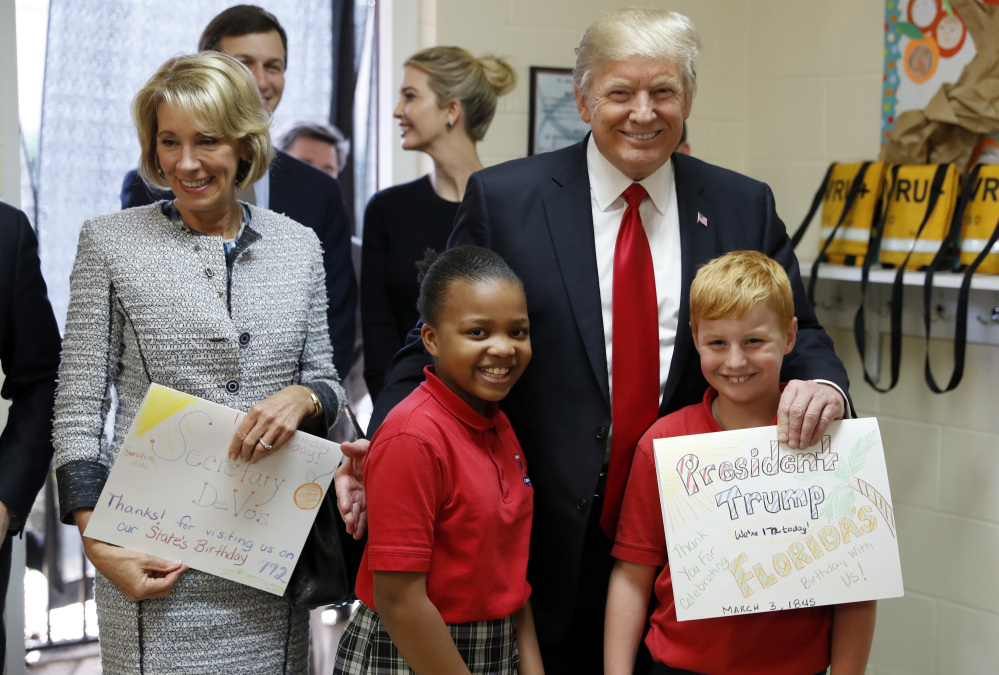 Associated Press/Alex Brandon
President Trump and Education Secretary Betsy DeVos pose with fourth graders Janayah Chatelier, 10, left, Landon Fritz, 10, after they received cards from the children, during a tour of Saint Andrew Catholic School last Friday.