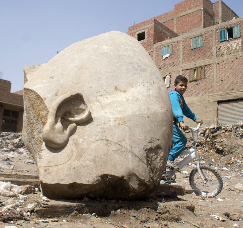 A boy rides his bicycle past a recently discovered statue in a Cairo slum that may be of pharaoh Ramses II, in Cairo, Egypt, on Friday.