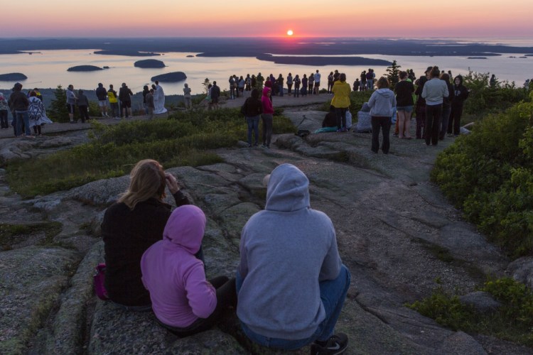 Hundreds of people gather atop Cadillac Mountain in Acadia National Park to watch the sun rise in June. The park's 100th anniversary contributed to Maine's jump in tourism in 2016.