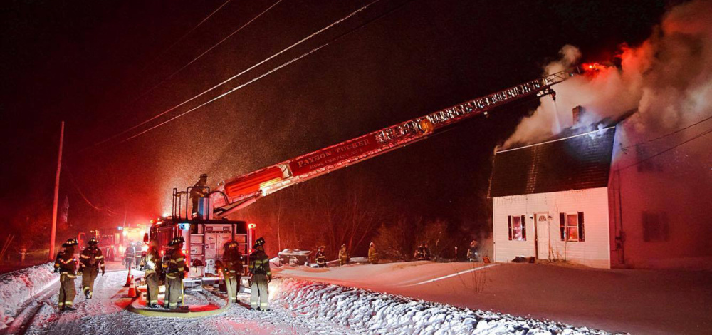 Firefighters from Winthrop use a ladder truck late Tuesday to spray a stream of water through an opening in the roof of a home at 554 Route 135 in Monmouth. "Everyone was just encrusted with ice," said Monmouth Fire Chief Dan Roy.