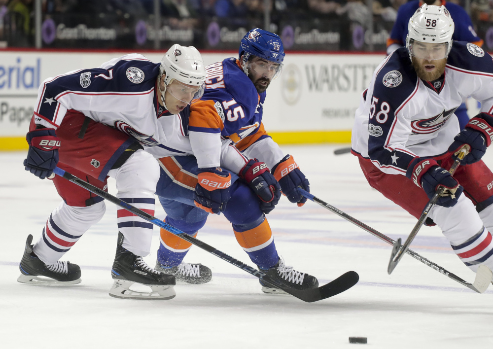 Blue Jackets defensemen Jack Johnson, left, and David Savard, right, look to keep the puck out of the reach of Islanders right wing Cal Clutterbuck during a 3-2 overtime win for Columbus Saturday in New York.