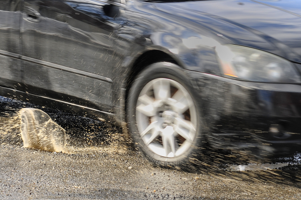 A car splashes through a pothole at the corner of Water and Bridge streets, a section plagued by the holes in Gardiner.
