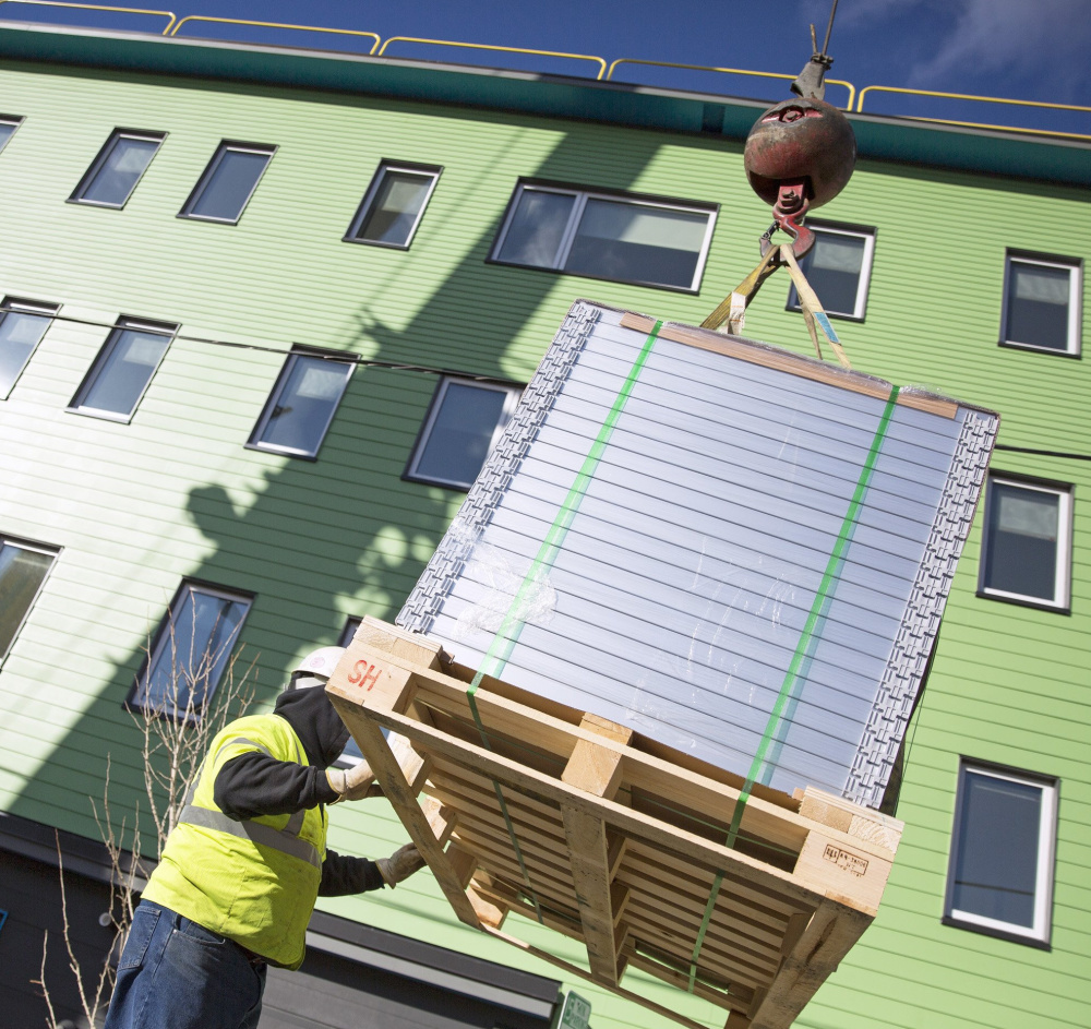 Dave Cleveland, of Keeley Crane Service, guides a pallet of solar panels as they are lifted to the roof in Portland.
