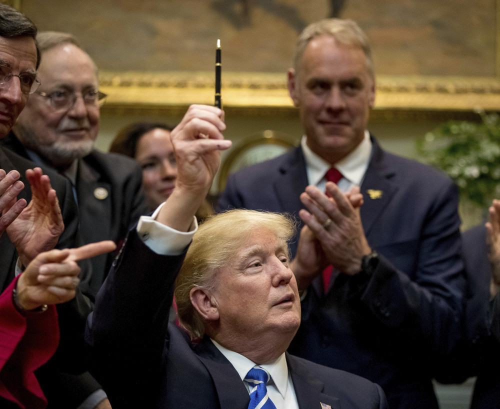 President Trump holds up the pen he used to sign a bill in the Roosevelt Room of the White House on Monday. From left are Sen. Tom Barrasso, R-Wyo., Rep. Don Young, R-Alaska, and Interior Secretary Ryan Zinke.