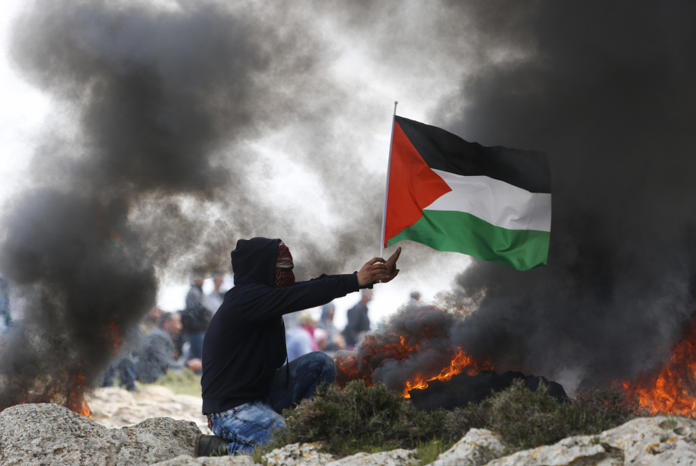 A protester holds a Palestinian flag as smoke rises from burning tires during clashes with Israeli security forces near the West Bank city of Ramallah last week.