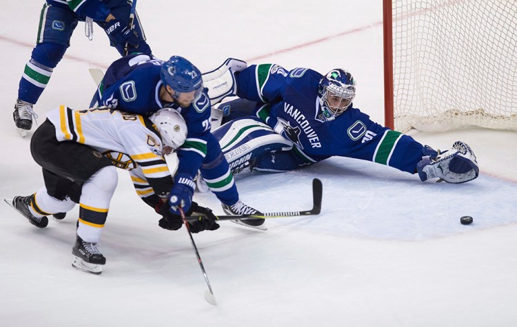 Boston Bruins left wing Brad Marchand scores against Vancouver Canucks goalie Ryan Miller while being checked by Canucks defenseman Alexander Edler during the third period of Monday night's game  in Vancouver.
