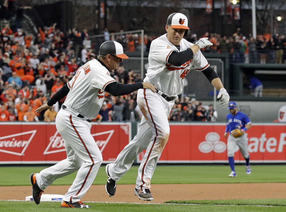 Baltimore third-base coach Bobby Dickerson, left, celebrates with Mark Trumbo as he rounds third base after his solo homer in the 11th inning the Orioles' 3-2 win over Toronto on Monday.