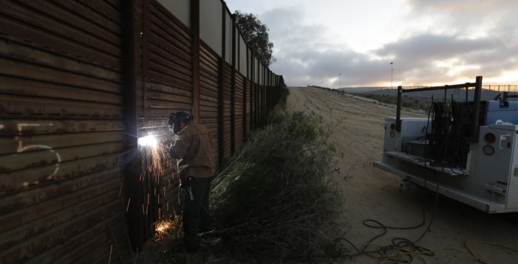 A U.S. Border Patrol agent welds a section of steel over a hole cut in the existing border wall in San Diego in 2013. Bids on the first design contracts for a full wall, due Tuesday, show companies are preparing for the worst if they get the potentially lucrative but controversial job.