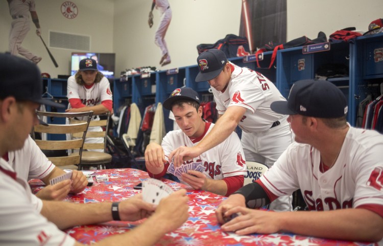 There are many ways to pass the time in the clubhouse as Teddy Stankiewicz leans over and helps Jordan Procyshen play his hand in a card game in the Sea Dog's clubhouse at Hadlock Field on Tuesday.