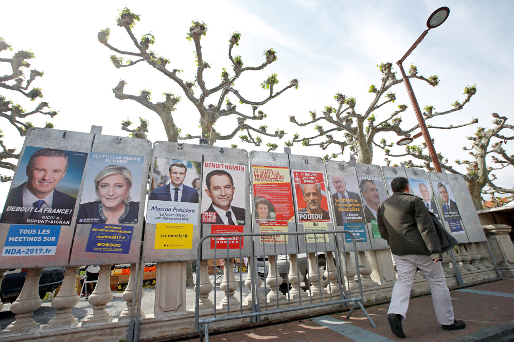 A man walks past campaign posters of the 11 candidates in Sunday's French presidential election, in Le Soler, France. The shadow over the EU's future comes in the form of not one but two candidates – far-right nationalist Marine Le Pen, second from left, and left-wing populist Jean-Luc Melenchon, third from right. Standing in the way of an EU meltdown: centrist Emmanuel Macron, third from left.