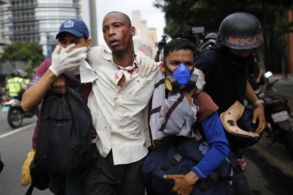 Paramedics assist a man injured during clashes with security forces during protests asking for the resignation of President Nicolas Maduro in Caracas, Venezuela, on Thursday. Tens of thousands of protesters flooded the streets in the biggest anti-government demonstrations in years.