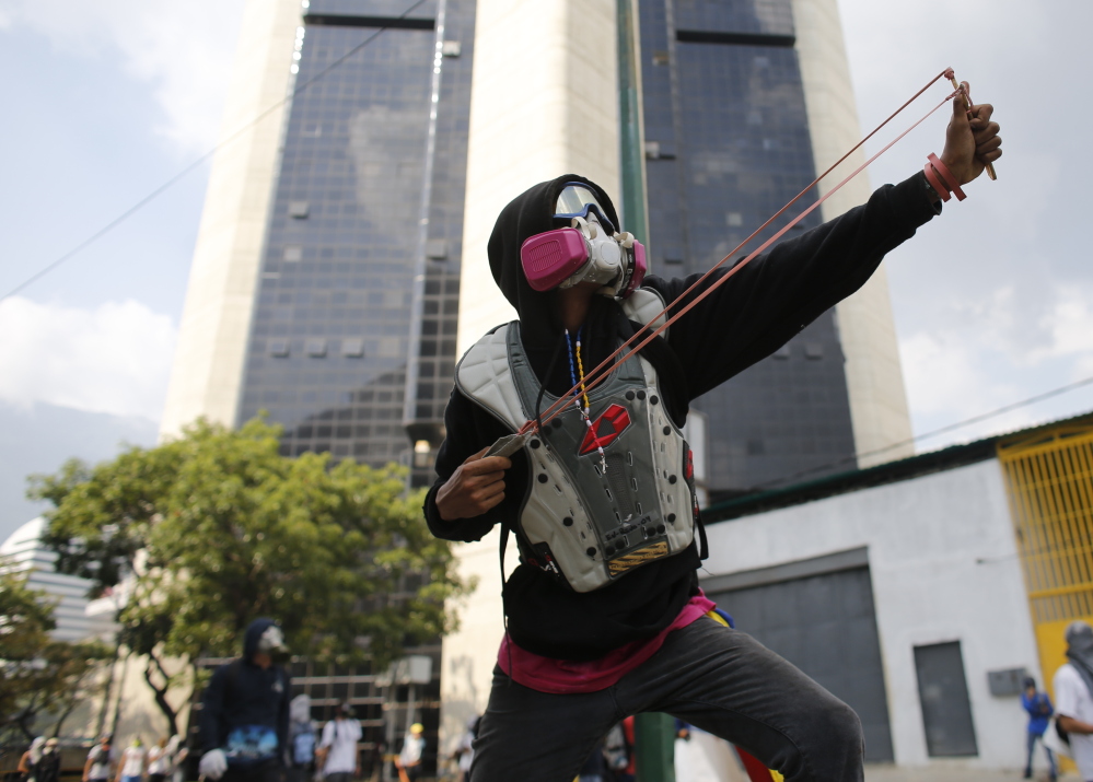 An opponent of President Nicolas Maduro aims his slingshot as security forces block protesters from reaching the national ombudsman office in Caracas.