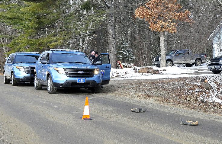 Two Maine State Troopers consult outside a residence on the Winnecook Road in Burnham while investigating the death of a woman on Sunday. A pair of  boots are in the road in the foreground.