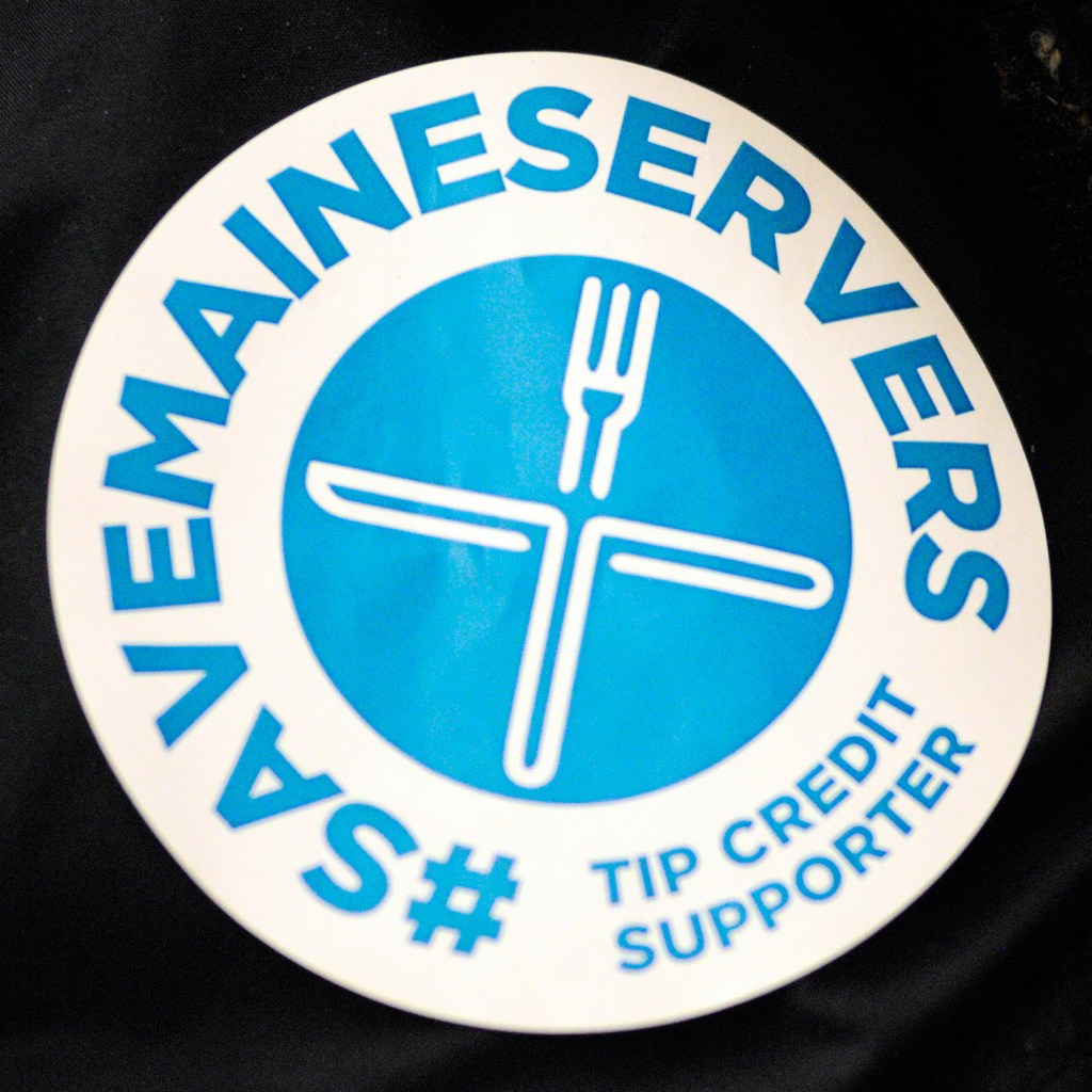Supporters of changes to Maine's tip credit rules wore blue stickers for Wednesday's legislative hearing.