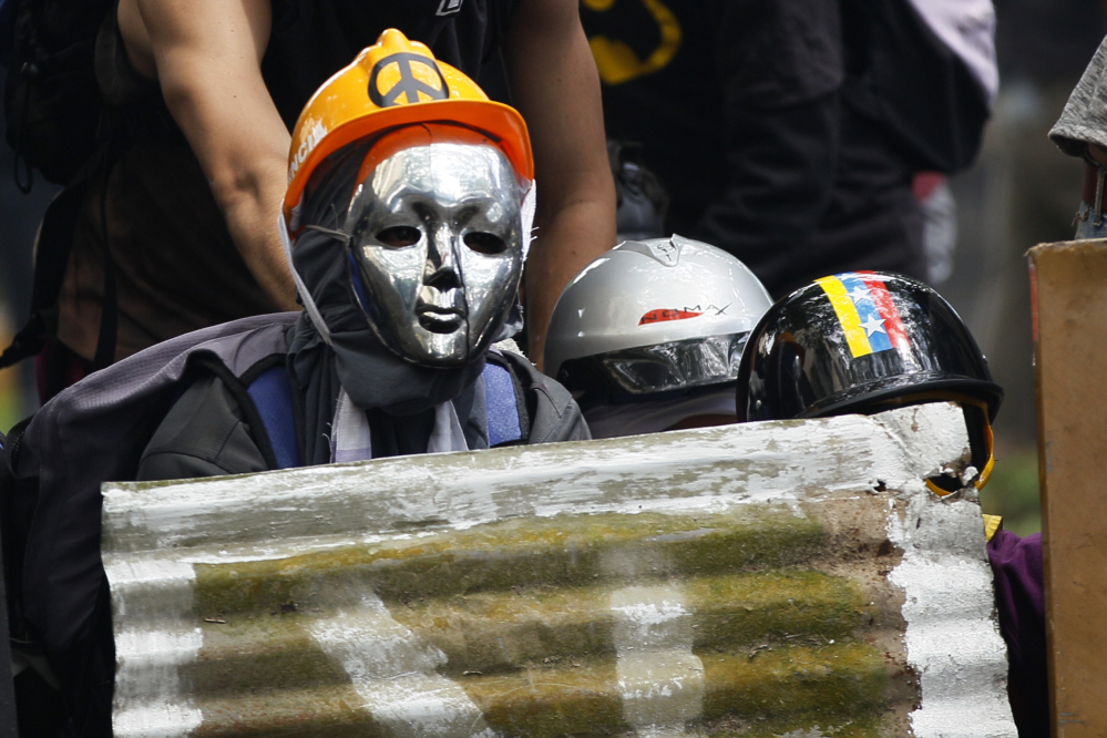 Masked demonstrators take cover during clashes with security forces at an opposition May Day march in Caracas, Venezuela, on Monday.