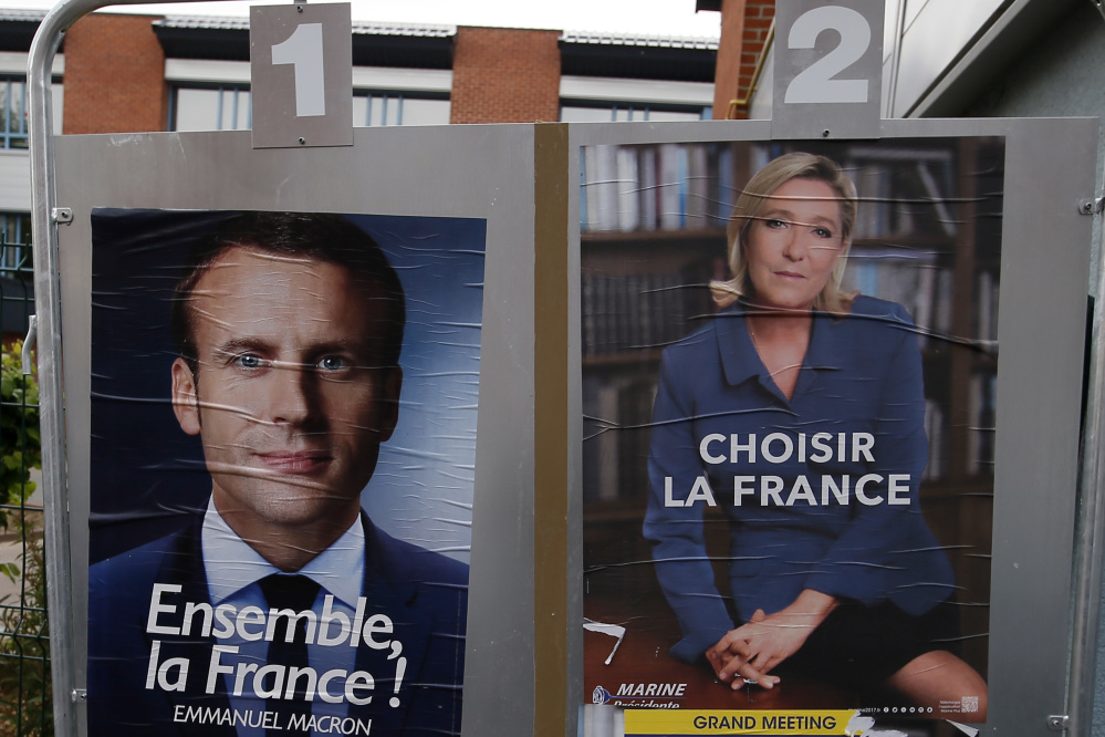 Election campaign posters for French centrist presidential candidate Emmanuel Macron and far-right candidate Marine Le Pen are displayed in front of the polling station where Le Pen will vote in Henin Beaumont, northern France.