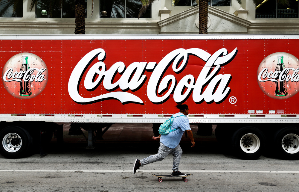 A skateboarder rides past a Coca-Cola sign on a delivery truck in Miami Beach, Fla, last fall. The company is investing in new, healthier brands, slashing expenses and offloading bottling plants around the world.
