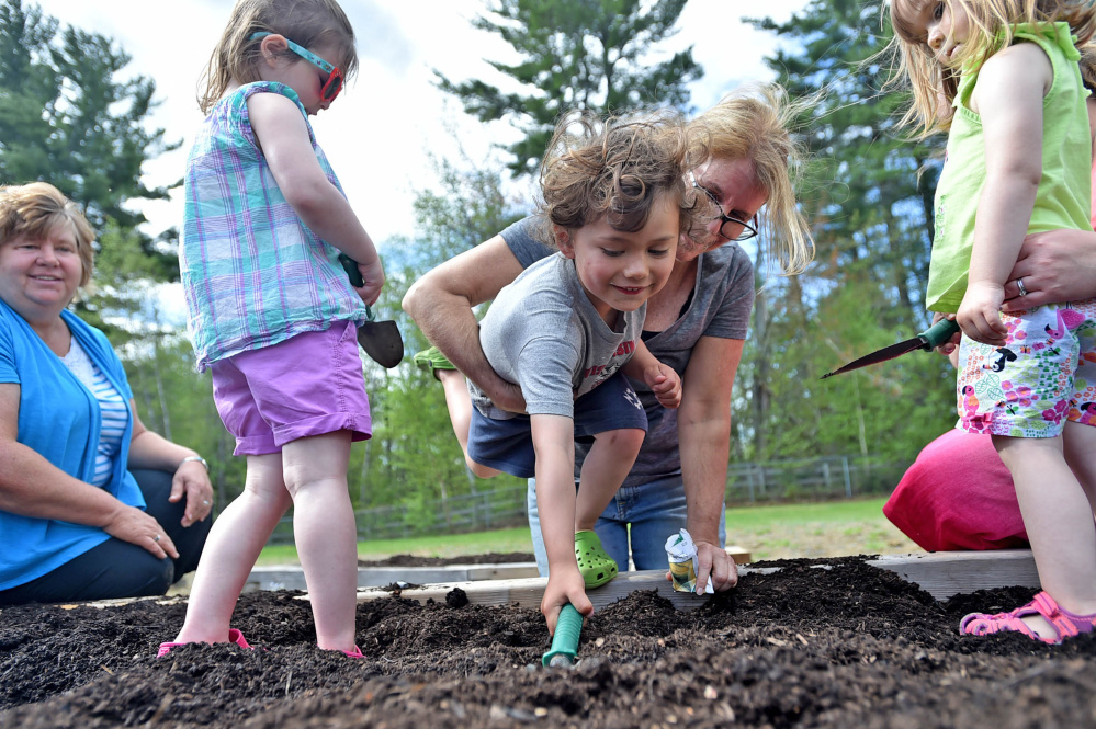 Mary Mayhew, state commissioner of the Department of Health and Human Services, center, helps Balin Irving, 3, drop a squash seed at the Sprouts preschool program in Unity. Mya Robertson, 3, left, and Anna Ford, 3, help dig holes in the soil.