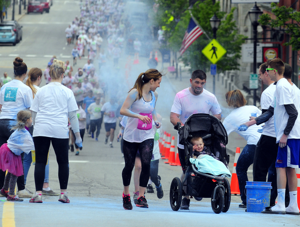 Kristin and Josh DuBois and their son Ethan, of Belgrade, continue their run Saturday after passing through blue powder at the first color station on Water Street during a 5K Color Dash race in Augusta.