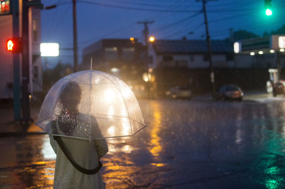 A woman walks down Washington Avenue in Portland with her umbrella as the rain begins to fall at dusk Monday.