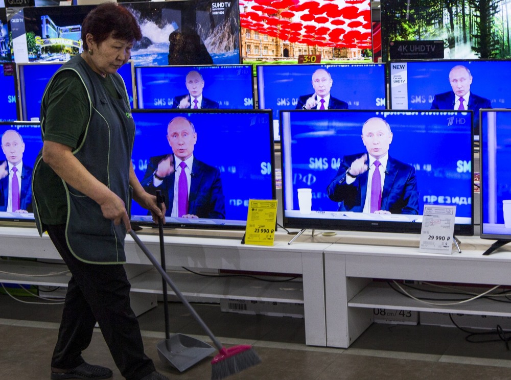 A worker passes TVs showing Russian President Vladimir Putin at his call-in show on Thursday in Moscow. Popular for his global role, his handling of corrupt officials is criticized.