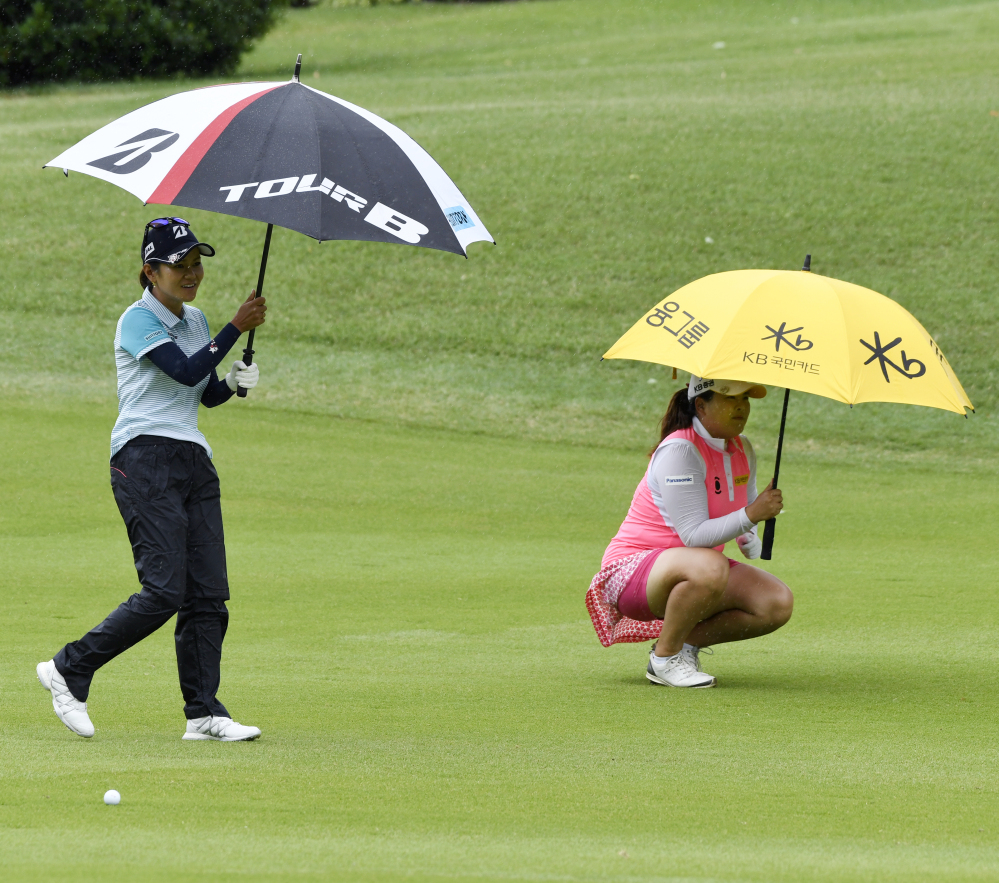 Ai Miyazato, left, of Japan, and Inbee Park, of South Korea, try to stay dry as it begins to rain while playing the second hole Friday during the LPGA Wal-Mart NW Arkansas Championship tournament at Pinnacle Country Club in Rogers, Ark.