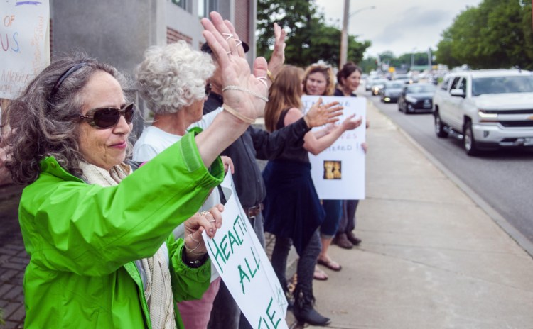 Leah Postman, left, of Winthrop waves to passing drivers after one of them honked during a health care demonstration Friday in front of the Edmund S. Muskie Federal Building on Western Avenue in Augusta.