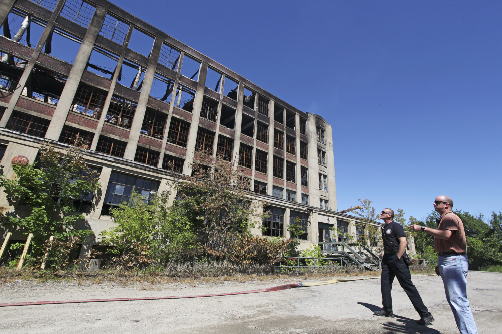 Sanford Fire Chief Steve Benotti and firefighter Todd Levesque survey the still-smoldering mill  building on Sunday. The city now plans to seek state and federal funding to help with the cleanup.