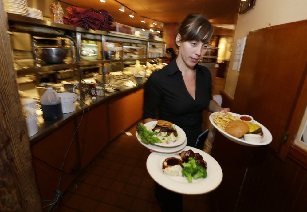 A waitress at a Seattle restaurant carries food to a table in 2014. A new study finds that low-wage workers may not benefit overall from an increase in the minimum wage, but the study does not include larger employers.
