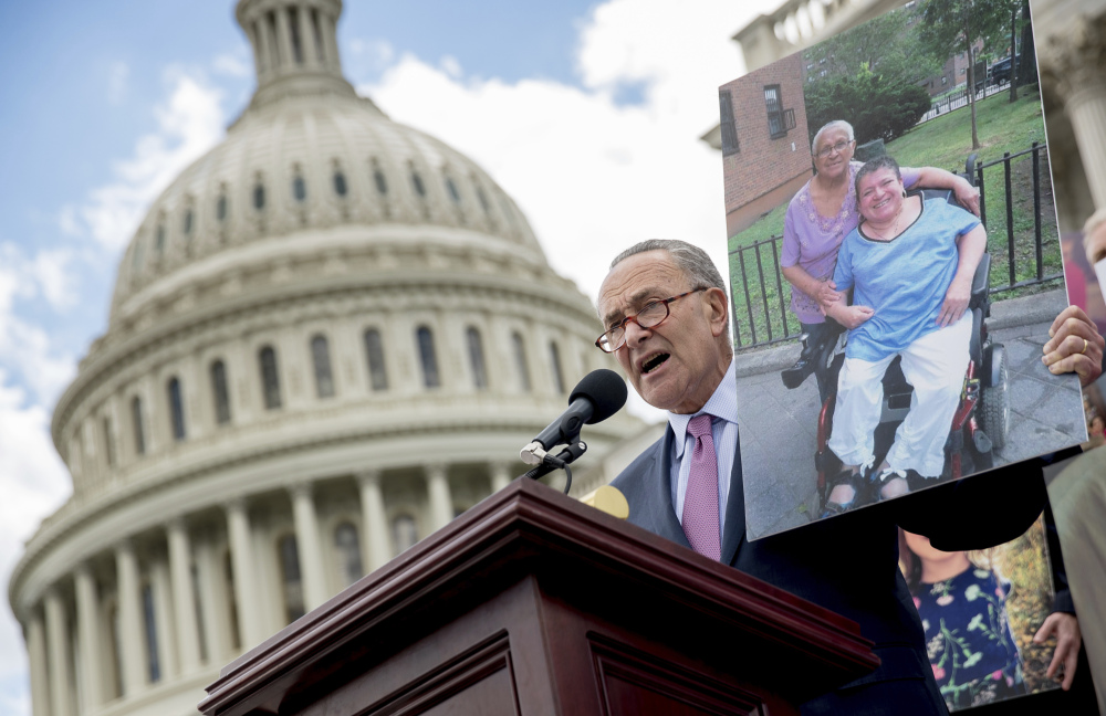 Senate Minority Leader Sen. Chuck Schumer of New York holds up a photograph of constituents who would be adversely affected by the proposed Republican Senate health care bill as he and Democratic senators speak outside the Capitol Building in Washington on Tuesday.