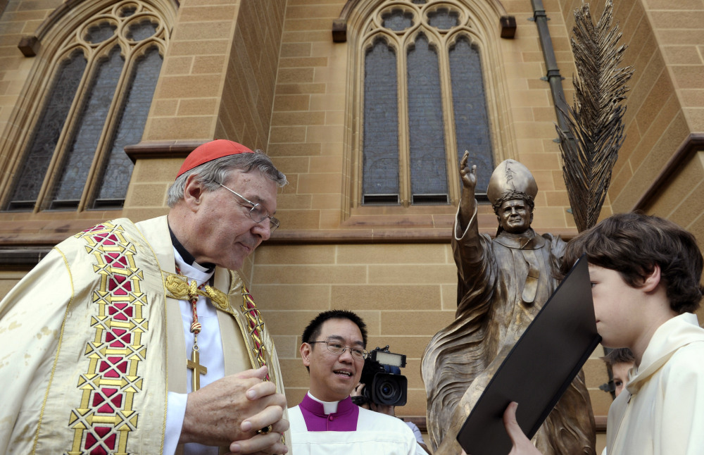 Cardinal George Pell, left, reads a Bible during the blessing of a statue of John Paul II at St Mary's Cathedral in Sydney, Australia, in 2011. Pell faces multiple charges of “historical sexual assault offenses,” meaning offenses that generally occurred in the past.