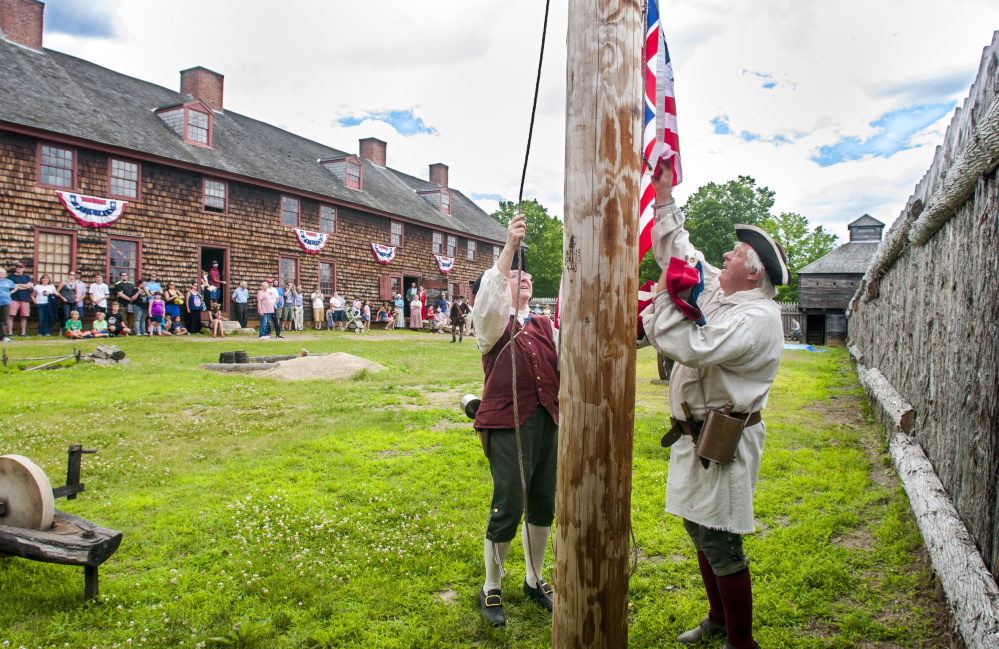 Re-enactors Jackie Fournier, left, and Stan Novak take down a Grand Union flag and swap it for one with thirteen stars and stripes Tuesday at Old Fort Western in Augusta.