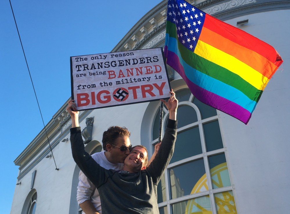 Nick Rondoletto, left, and Doug Thorogood, a couple from San Francisco, wave a rainbow flag and hold a sign against a proposed ban of transgendered people in the military at a protest in the Castro District on Wednesday in San Francisco.