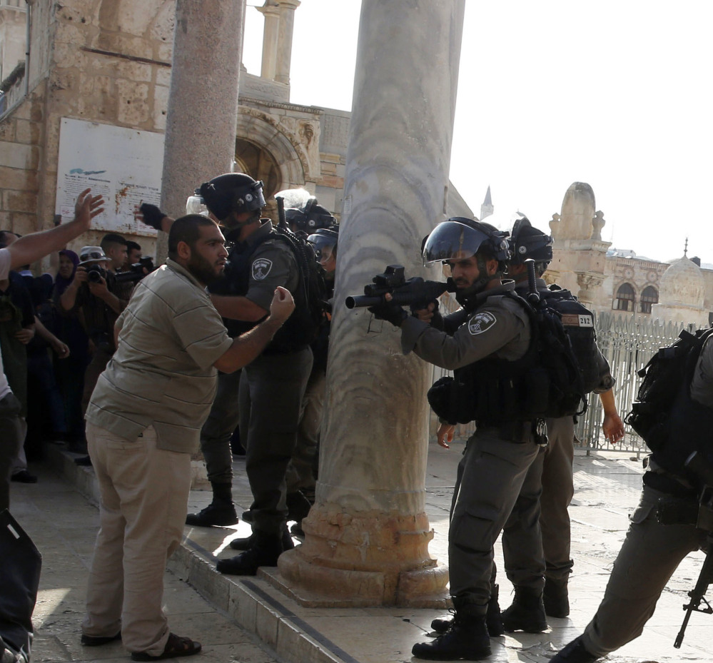 An Israeli police officer aims his gun at Palestinians during clashes Thursday at the Al-Aqsa Mosque compound  in Jerusalem's Old City. Mass protests are expected for Friday prayers, the highlight of the Muslim religious week.